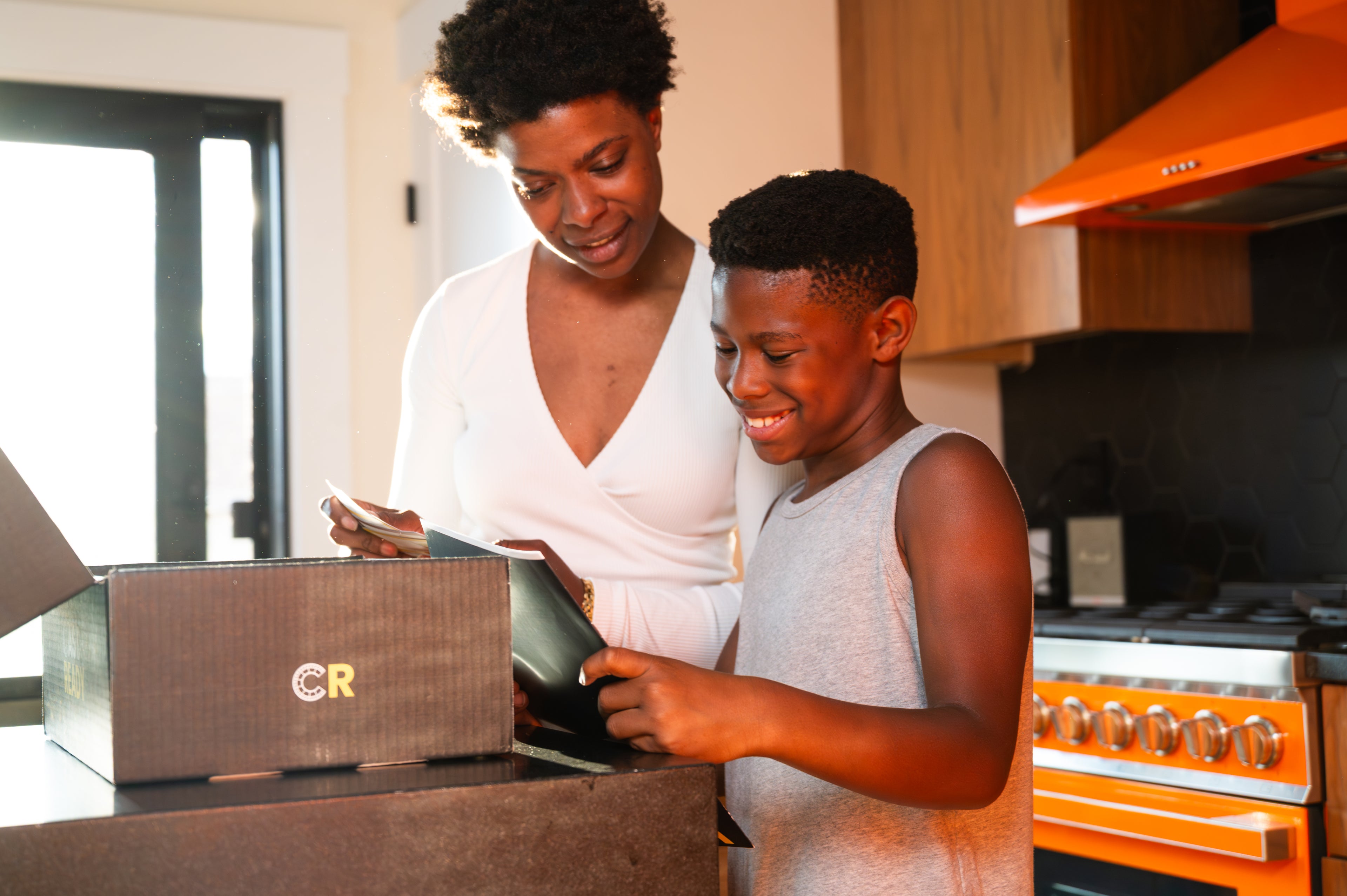 Mother and son opening a CastReady acting education kit together in their home kitchen, smiling and engaged.